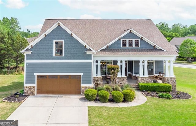 craftsman-style house with a porch, driveway, stone siding, a front yard, and an attached garage
