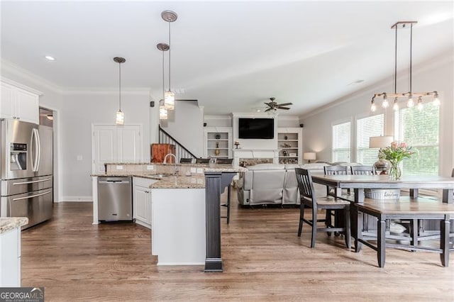 kitchen with a sink, stainless steel appliances, a ceiling fan, white cabinetry, and ornamental molding