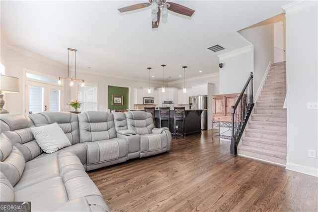 living room featuring wood finished floors, stairs, ceiling fan, visible vents, and crown molding