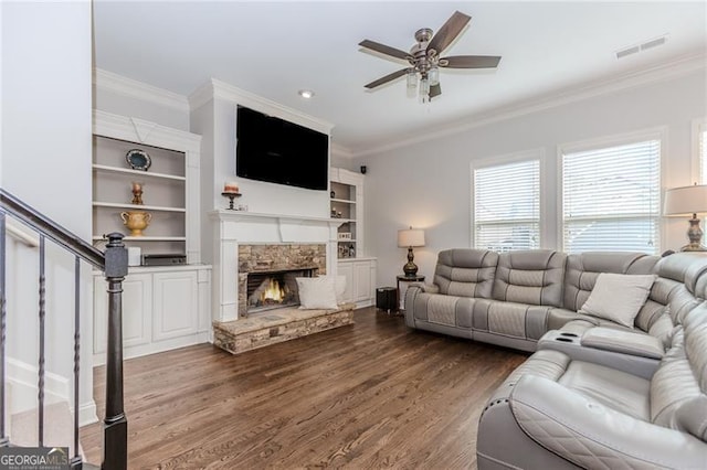 living room featuring ceiling fan, a stone fireplace, dark wood-style flooring, visible vents, and crown molding