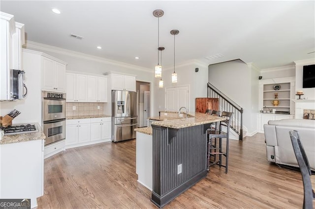 kitchen with appliances with stainless steel finishes, white cabinets, ornamental molding, visible vents, and open floor plan