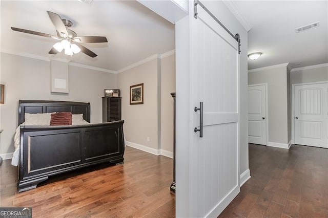 bedroom featuring wood finished floors, a barn door, crown molding, and visible vents