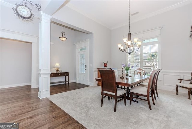 dining space with crown molding, an inviting chandelier, decorative columns, and wood finished floors