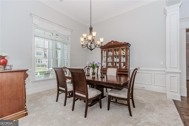 carpeted dining space with crown molding, a notable chandelier, and ornate columns