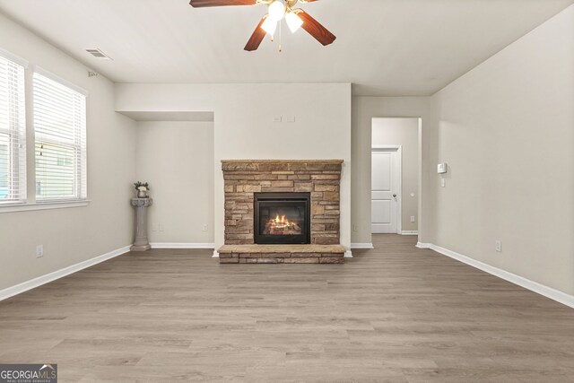 15 Manas Ct, Covington, GA 30016 - unfurnished living room with light wood-type flooring, a ceiling fan, visible vents, a stone fireplace, and baseboards