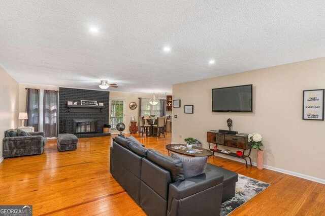 4393 Housworth Dr, Stonecrest, GA 30038 - living area featuring a textured ceiling, ceiling fan, light wood-type flooring, and a brick fireplace
