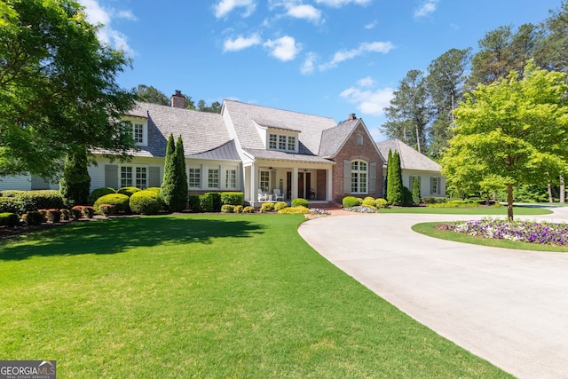new england style home with a front yard, a standing seam roof, covered porch, a chimney, and curved driveway