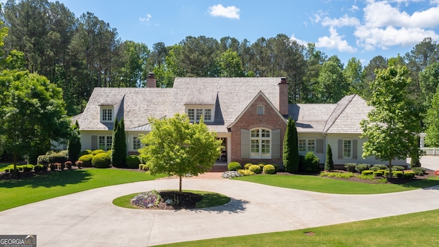 cape cod-style house featuring a chimney, a front lawn, and curved driveway