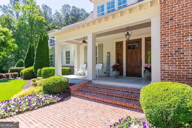 entrance to property with ceiling fan, a porch, and brick siding