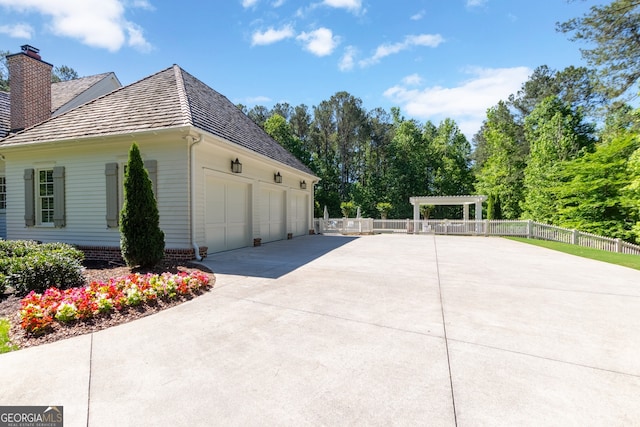 view of side of property featuring a chimney, fence, a garage, and a pergola