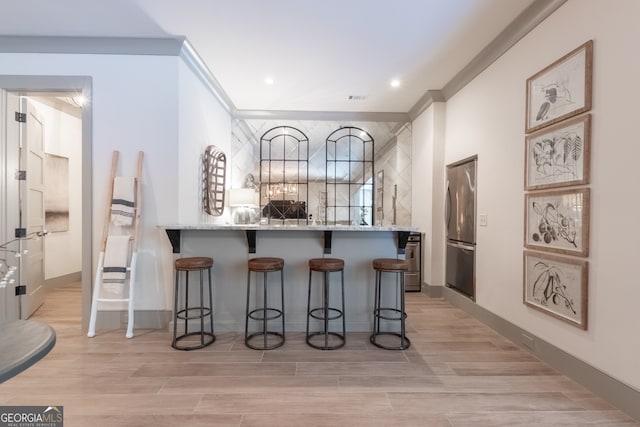bar with crown molding, light wood finished floors, visible vents, and freestanding refrigerator
