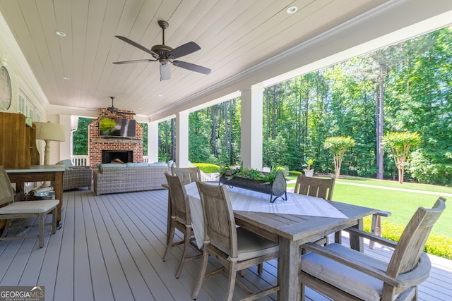 wooden terrace with a lawn, outdoor dining space, ceiling fan, and an outdoor living space with a fireplace