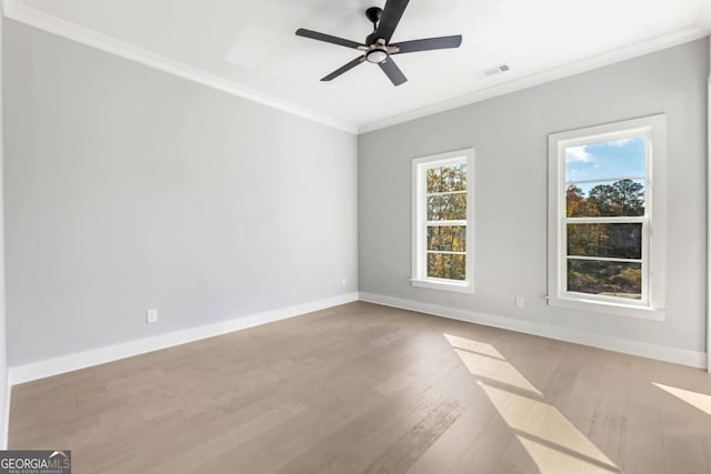 empty room featuring baseboards, visible vents, wood finished floors, and crown molding
