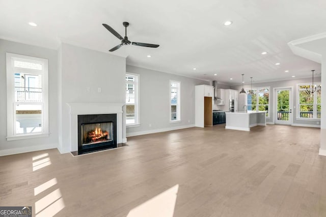 unfurnished living room featuring light wood finished floors, a healthy amount of sunlight, a lit fireplace, and baseboards