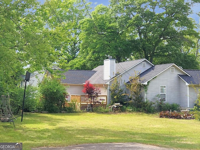 exterior space with roof with shingles, a deck, a front lawn, and a chimney