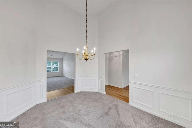 unfurnished dining area featuring carpet flooring, a notable chandelier, a wainscoted wall, a decorative wall, and high vaulted ceiling