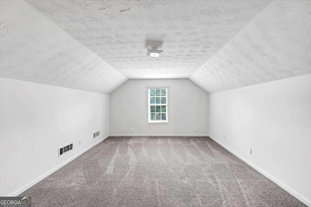 additional living space with visible vents, a textured ceiling, carpet floors, and vaulted ceiling