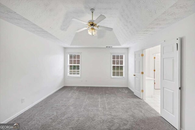 carpeted spare room with a textured ceiling, ceiling fan, a raised ceiling, and baseboards