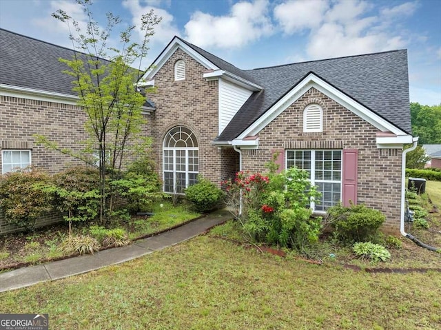 traditional-style home with brick siding, a shingled roof, and a front yard