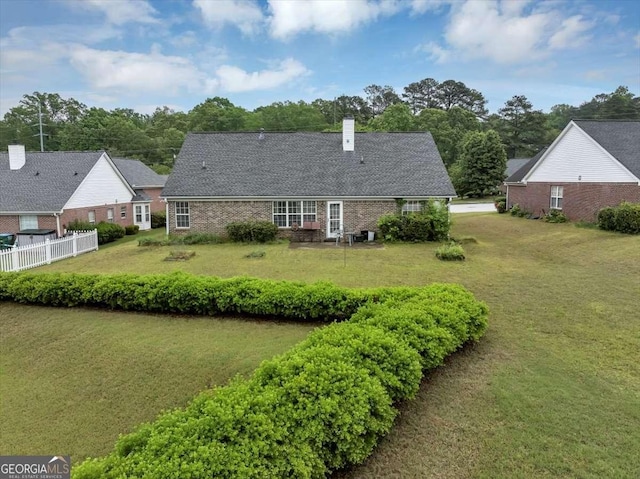 back of house featuring a chimney, brick siding, fence, and a yard