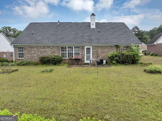 back of house featuring a chimney, a yard, brick siding, a shingled roof, and a patio area
