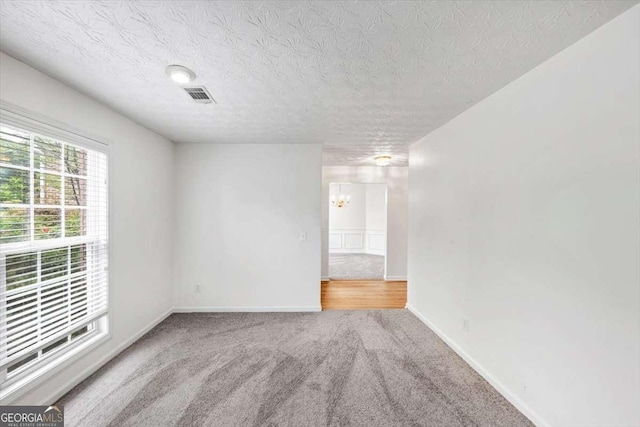 empty room with carpet floors, baseboards, visible vents, a notable chandelier, and a textured ceiling
