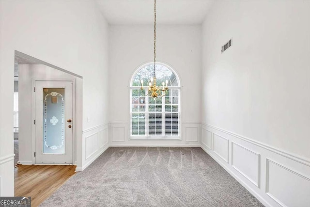 unfurnished dining area featuring visible vents, a decorative wall, a chandelier, and wainscoting