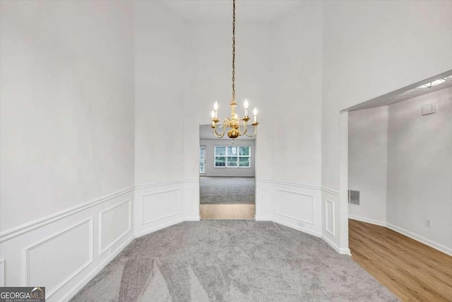unfurnished dining area with a chandelier, visible vents, a wainscoted wall, a towering ceiling, and a decorative wall