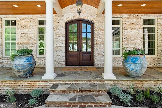 property entrance with a porch, french doors, and brick siding