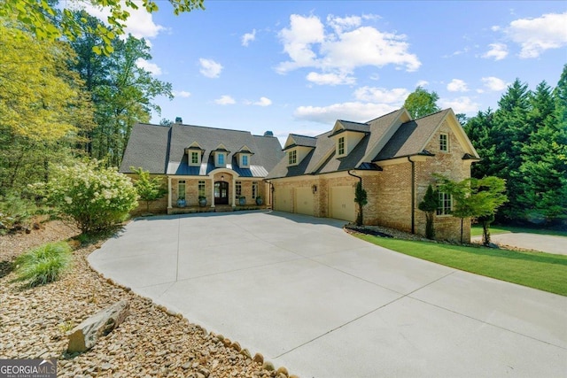 french country style house with driveway, an attached garage, and brick siding