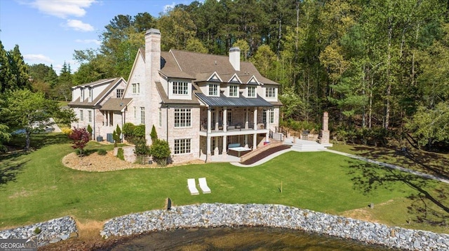 rear view of house with a standing seam roof, a yard, a patio area, and a chimney