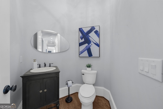 half bath featuring wood finished floors, toilet, vanity, and baseboards