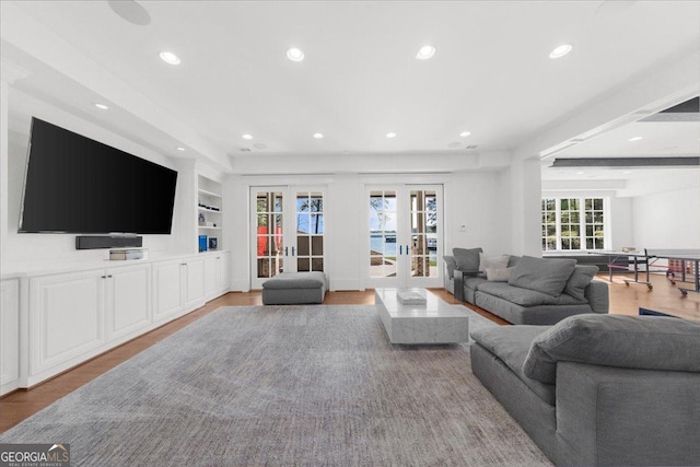 living room with built in shelves, recessed lighting, wood finished floors, and french doors