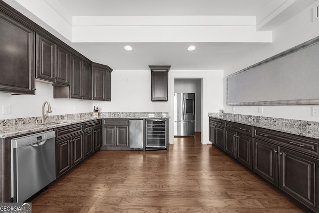 kitchen featuring a sink, appliances with stainless steel finishes, beverage cooler, dark brown cabinetry, and dark wood finished floors