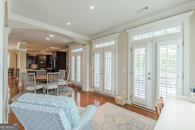 living room with ornamental molding, arched walkways, visible vents, and wood finished floors