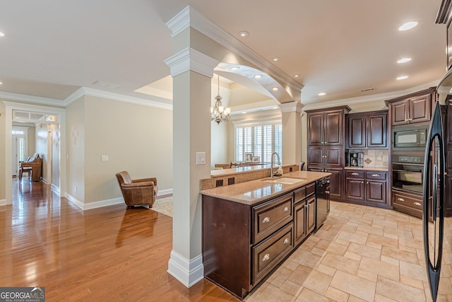 kitchen with light stone counters, black appliances, ornamental molding, a sink, and ornate columns