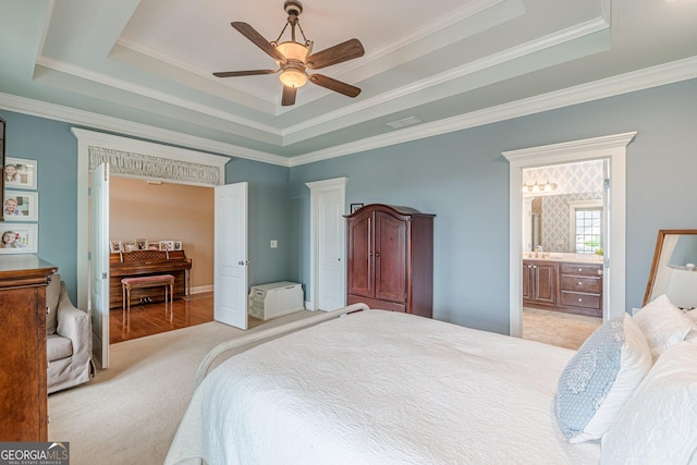 carpeted bedroom featuring a raised ceiling, a ceiling fan, crown molding, and ensuite bathroom