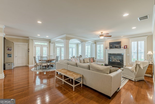 living room featuring ornamental molding, a ceiling fan, visible vents, and decorative columns