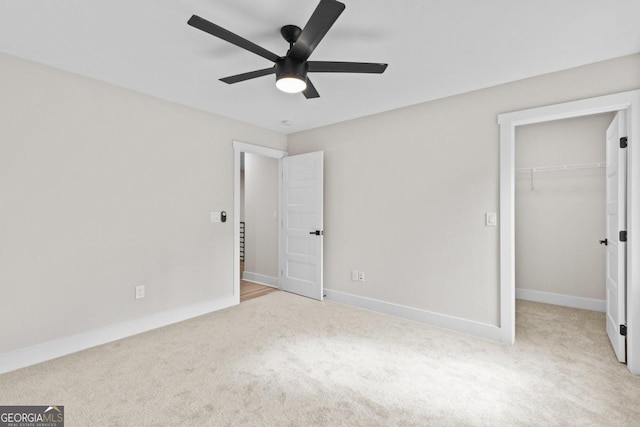 unfurnished bedroom with carpet flooring, a closet, a ceiling fan, a walk in closet, and baseboards