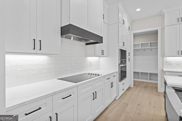 kitchen featuring black electric cooktop, light wood-type flooring, wall chimney exhaust hood, backsplash, and white cabinets