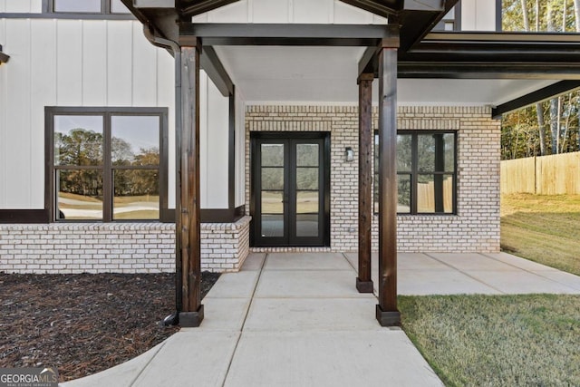 doorway to property with board and batten siding, fence, a yard, french doors, and brick siding