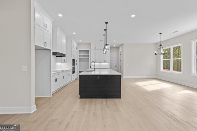 kitchen with a notable chandelier, light wood finished floors, a sink, and baseboards