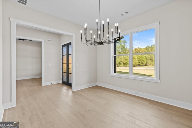 unfurnished dining area featuring an inviting chandelier, light wood-style flooring, french doors, and visible vents