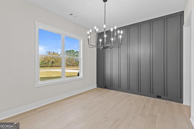 unfurnished dining area with an inviting chandelier, visible vents, light wood-type flooring, and a decorative wall