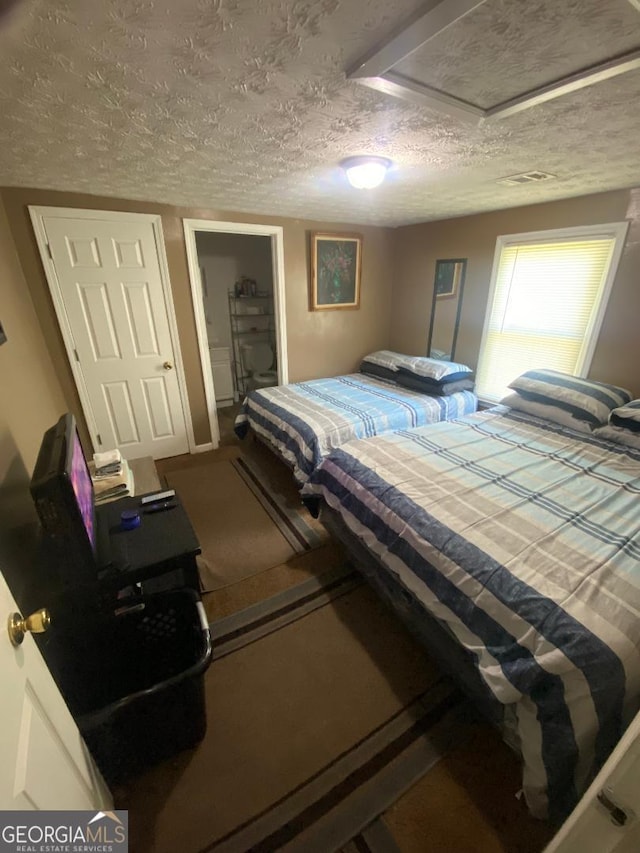 bedroom with a textured ceiling, visible vents, and attic access