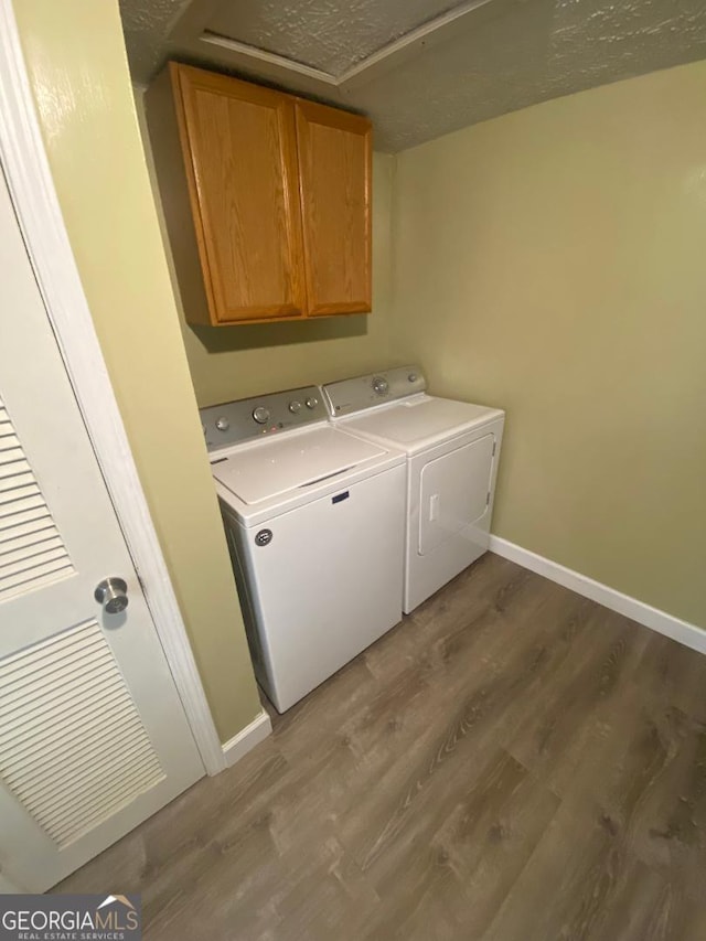 washroom featuring washer and dryer, baseboards, wood finished floors, and cabinet space