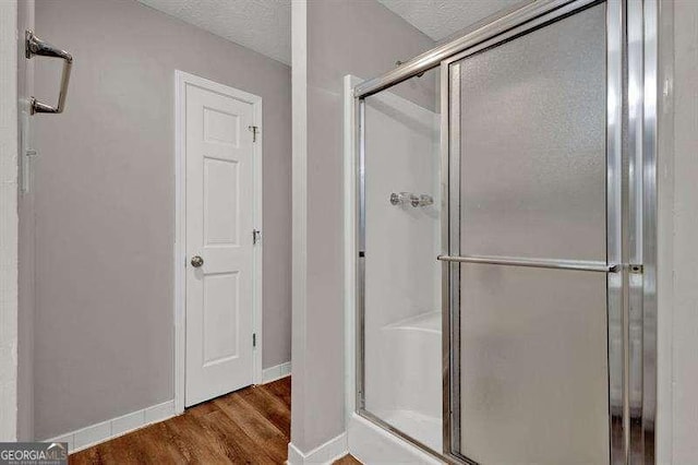 full bath featuring a textured ceiling, wood finished floors, a stall shower, and baseboards