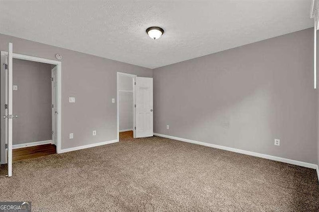 unfurnished bedroom with baseboards, carpet floors, a closet, a walk in closet, and a textured ceiling