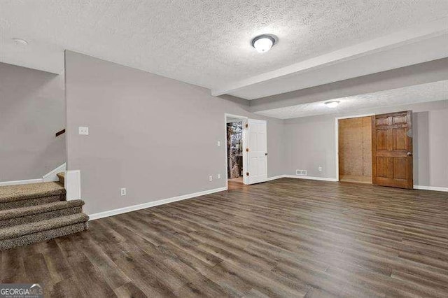 unfurnished living room with a textured ceiling, baseboards, beam ceiling, wood finished floors, and stairs