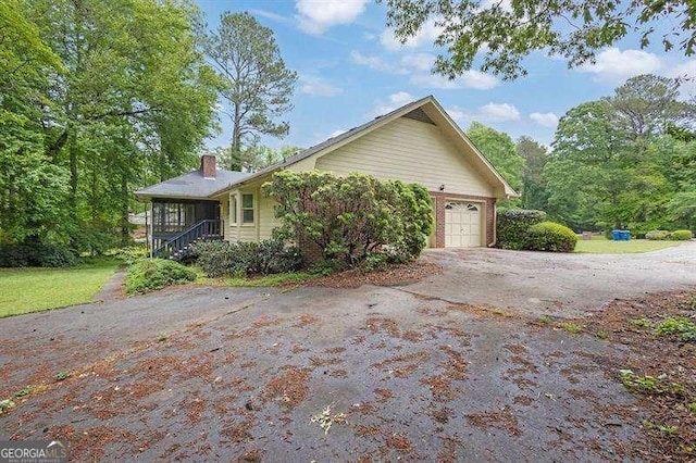 view of side of property featuring a chimney, driveway, and an attached garage